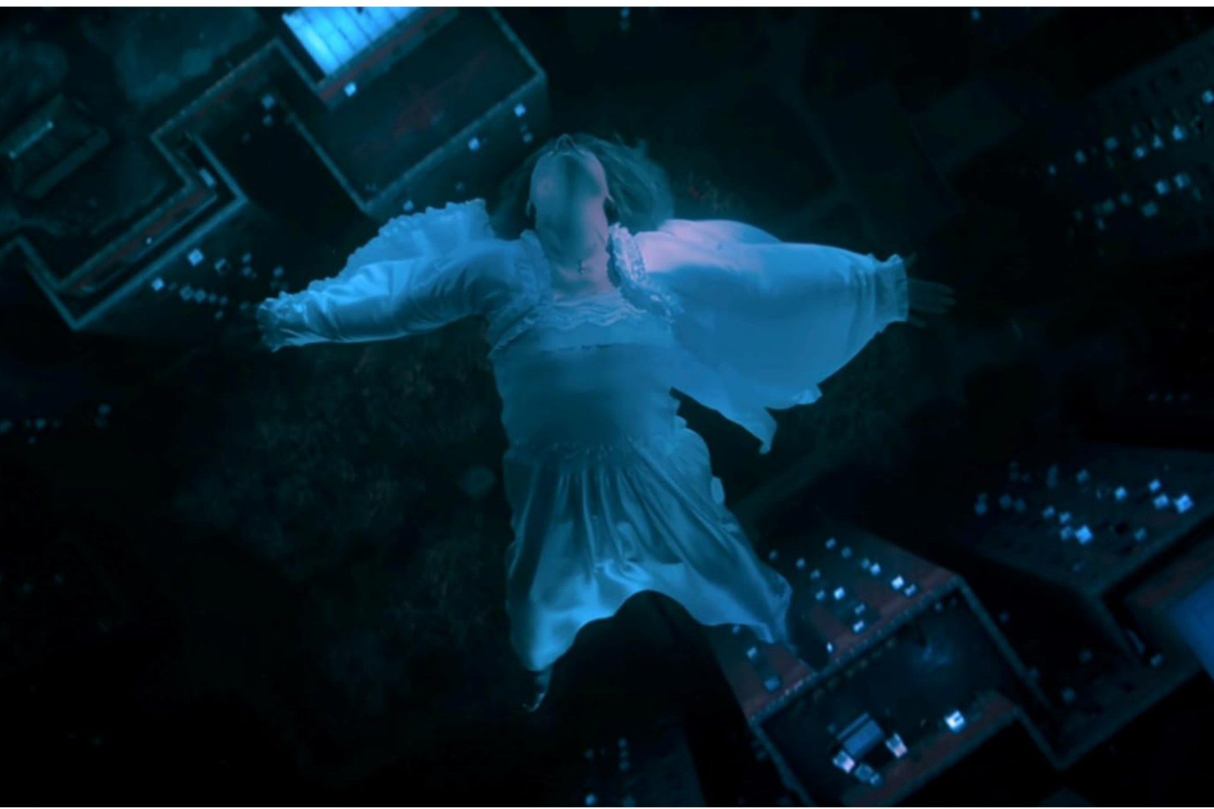 A woman in a flowing white dress appears to float or fall gracefully in a dimly lit urban nightscape, viewed from above.